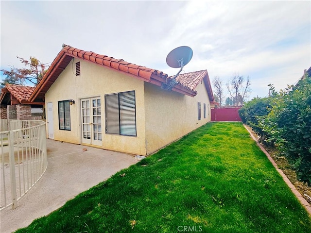 exterior space featuring a tile roof, stucco siding, a lawn, a patio area, and fence