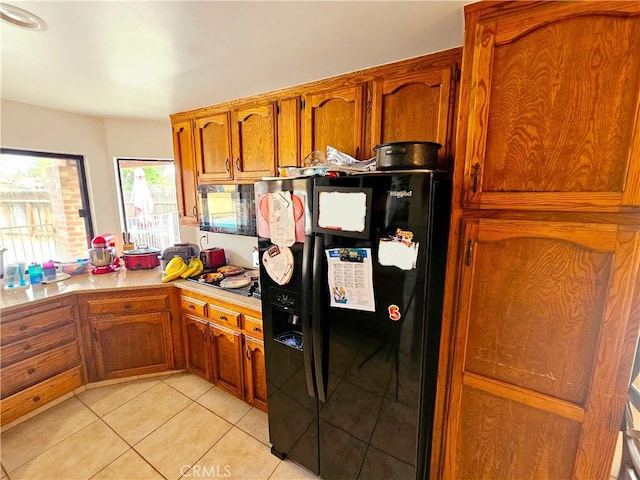 kitchen with brown cabinets, black appliances, light tile patterned floors, and light countertops