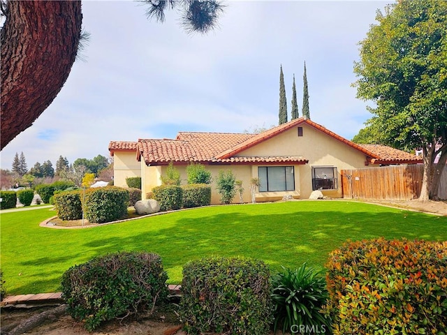 rear view of property featuring a yard, a tile roof, fence, and stucco siding