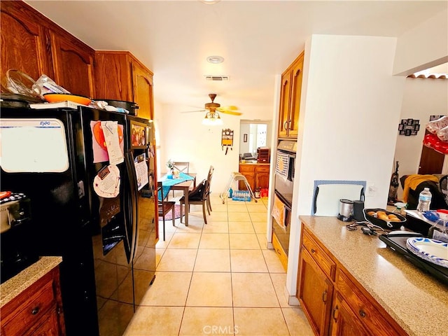 kitchen featuring light tile patterned floors, visible vents, wall oven, ceiling fan, and black fridge