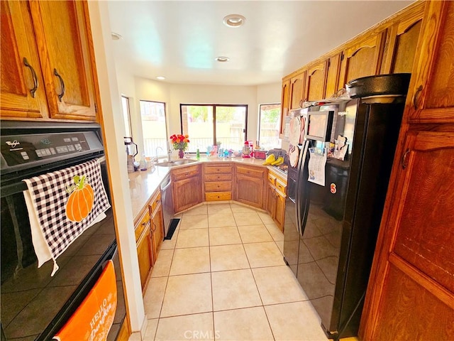 kitchen featuring black appliances, light tile patterned floors, brown cabinets, and a sink