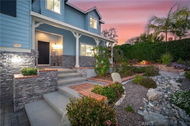 exterior entry at dusk featuring stone siding and covered porch