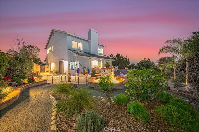 back of house at dusk featuring a chimney, fence, and stucco siding