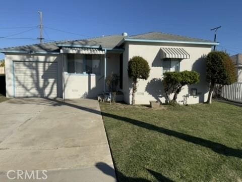 view of front facade with an attached garage, fence, concrete driveway, stucco siding, and a front yard