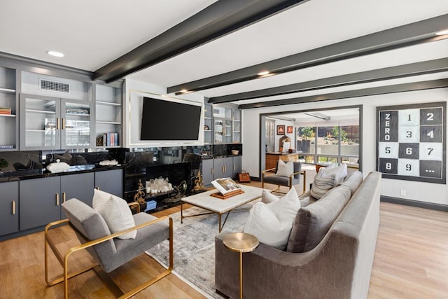 living room featuring light wood-style flooring, a fireplace, visible vents, and beamed ceiling