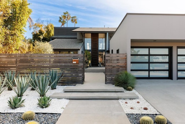 contemporary home with a garage, driveway, a fenced front yard, and stucco siding