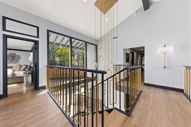 hall with high vaulted ceiling, light wood-style flooring, an upstairs landing, and baseboards