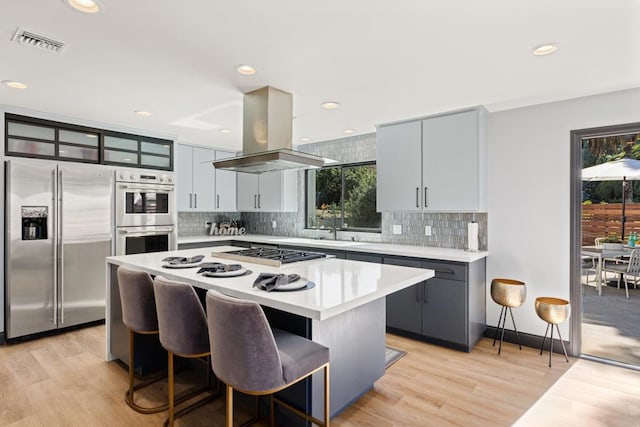 kitchen featuring visible vents, a center island, island exhaust hood, stainless steel appliances, and light countertops