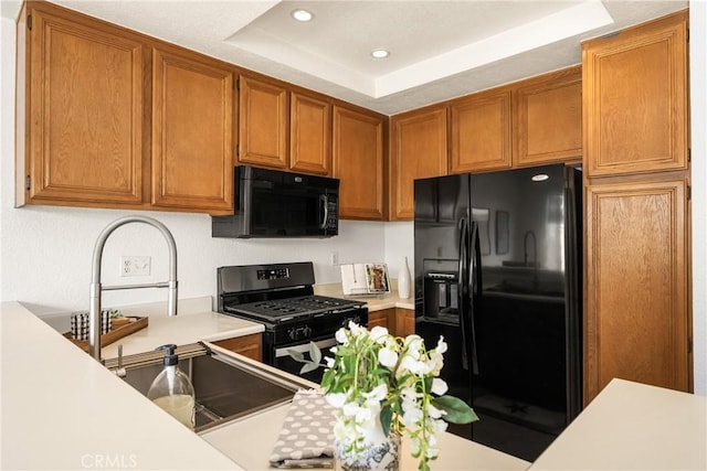 kitchen with brown cabinetry, a tray ceiling, light countertops, and black appliances