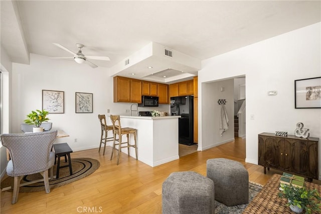 kitchen with black appliances, a peninsula, light wood-style flooring, and brown cabinets