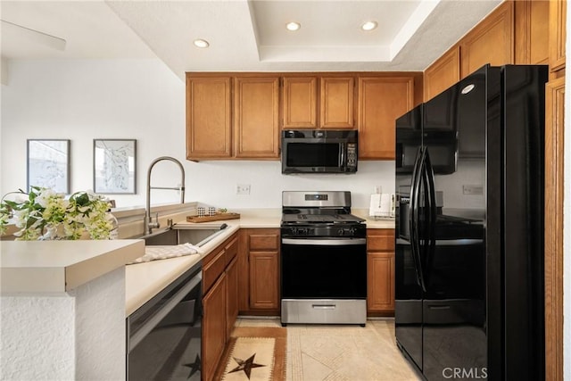 kitchen featuring a sink, light countertops, black appliances, a tray ceiling, and brown cabinetry