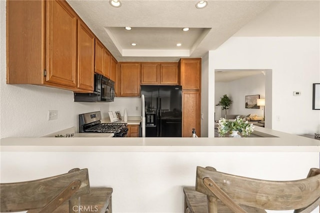 kitchen featuring a raised ceiling, a peninsula, light countertops, black appliances, and recessed lighting