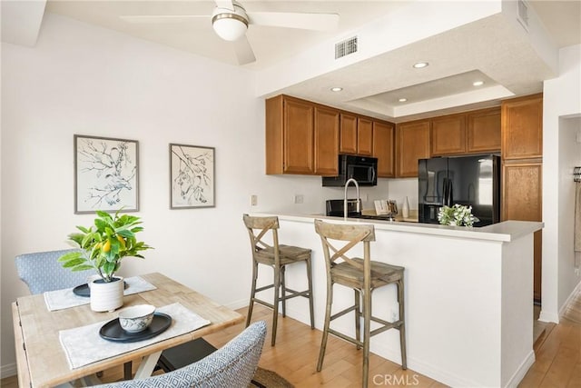 kitchen with black appliances, brown cabinetry, a peninsula, and visible vents