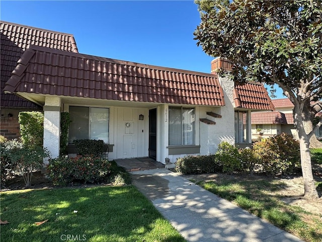 view of front of house with a tiled roof, a chimney, a front yard, and stucco siding