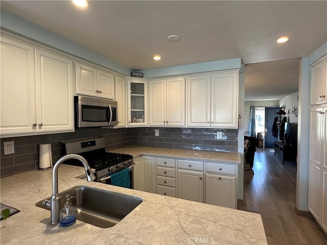 kitchen with stainless steel appliances, glass insert cabinets, a sink, and decorative backsplash