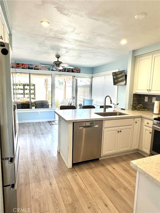 kitchen featuring stainless steel appliances, light countertops, light wood-style flooring, a sink, and a peninsula