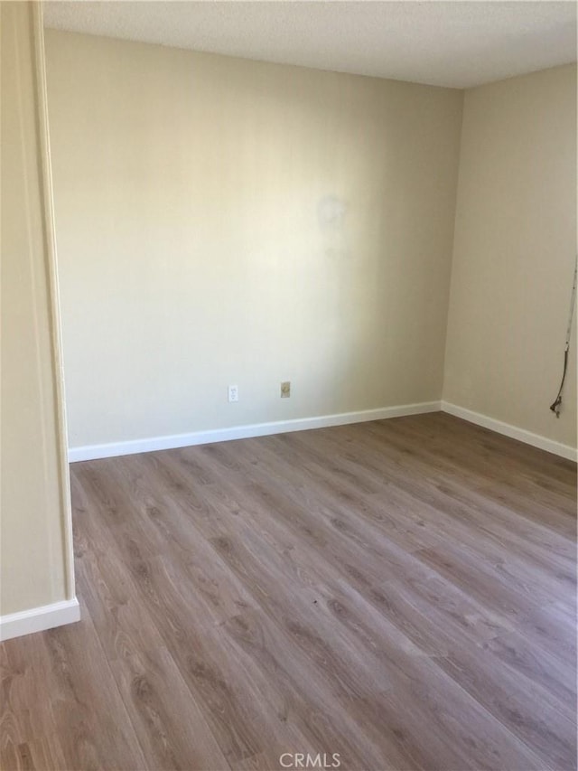 spare room featuring light wood-type flooring, baseboards, and a textured ceiling