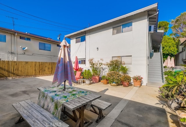 rear view of house with stucco siding, stairs, fence, and a patio