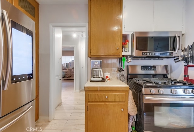 kitchen with brown cabinetry, decorative backsplash, tile countertops, appliances with stainless steel finishes, and white cabinetry