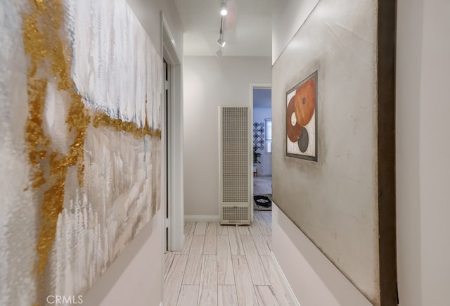 hall with rail lighting, baseboards, a heating unit, and light wood-style floors