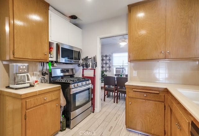 kitchen with tasteful backsplash, light wood-type flooring, light countertops, appliances with stainless steel finishes, and a ceiling fan