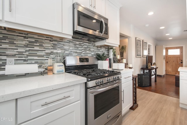 kitchen featuring white cabinets, decorative backsplash, light stone counters, stainless steel appliances, and light wood-style floors