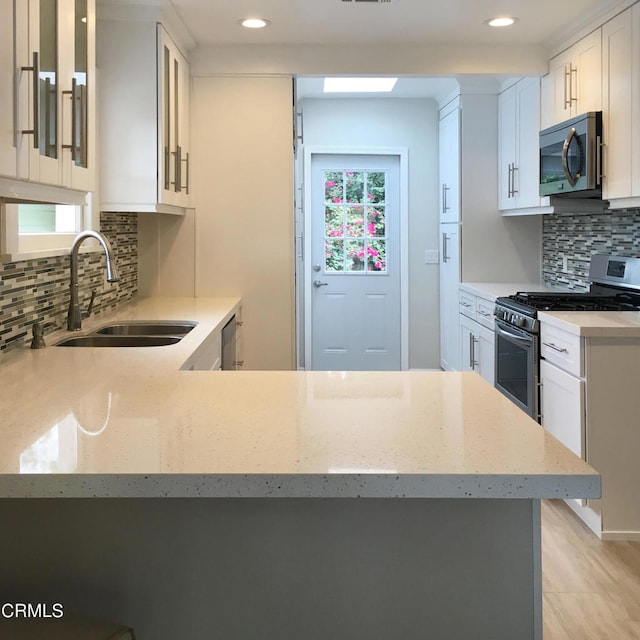 kitchen featuring glass insert cabinets, appliances with stainless steel finishes, a peninsula, white cabinetry, and a sink