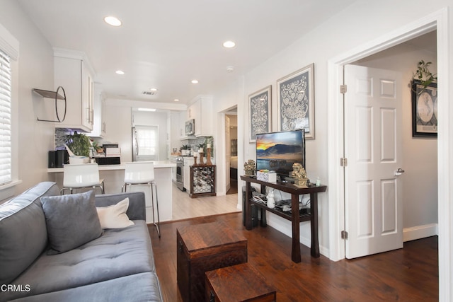 living area with dark wood-type flooring, recessed lighting, visible vents, and baseboards