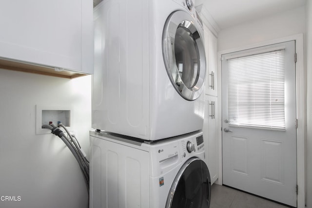 washroom featuring stacked washing maching and dryer, cabinet space, and tile patterned floors