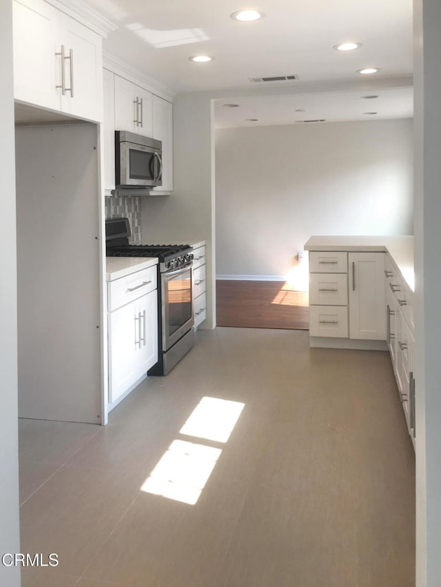 kitchen featuring visible vents, appliances with stainless steel finishes, light countertops, white cabinetry, and backsplash