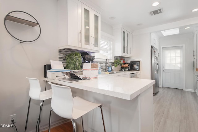 kitchen with a breakfast bar area, light countertops, glass insert cabinets, white cabinets, and a sink