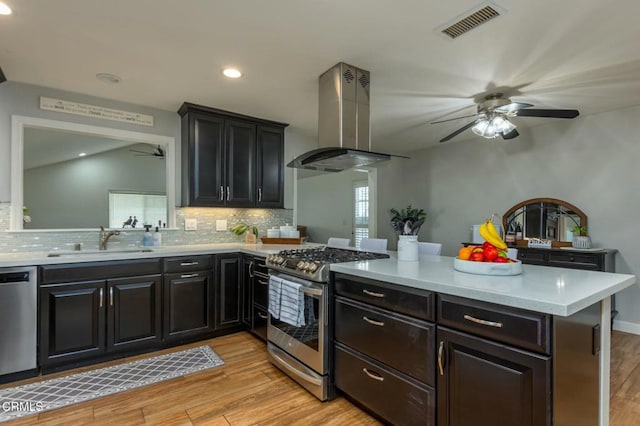 kitchen with light countertops, appliances with stainless steel finishes, a peninsula, and island exhaust hood