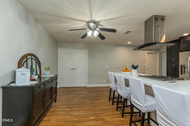 kitchen featuring dark brown cabinetry, visible vents, island range hood, appliances with stainless steel finishes, and wood finished floors