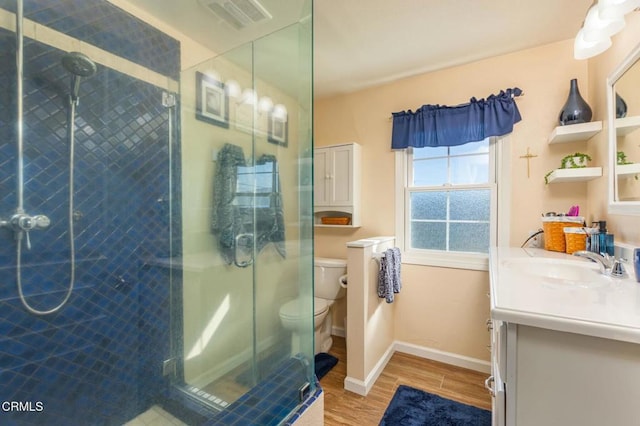 bathroom with toilet, a stall shower, vanity, wood finished floors, and baseboards