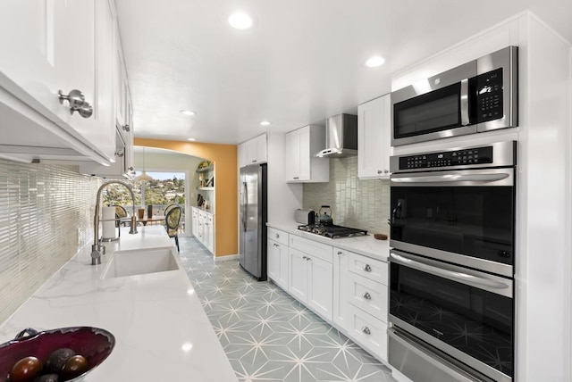 kitchen with wall chimney exhaust hood, appliances with stainless steel finishes, white cabinetry, and a sink