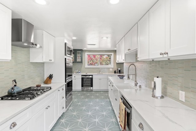 kitchen featuring appliances with stainless steel finishes, white cabinetry, wall chimney range hood, and light stone countertops