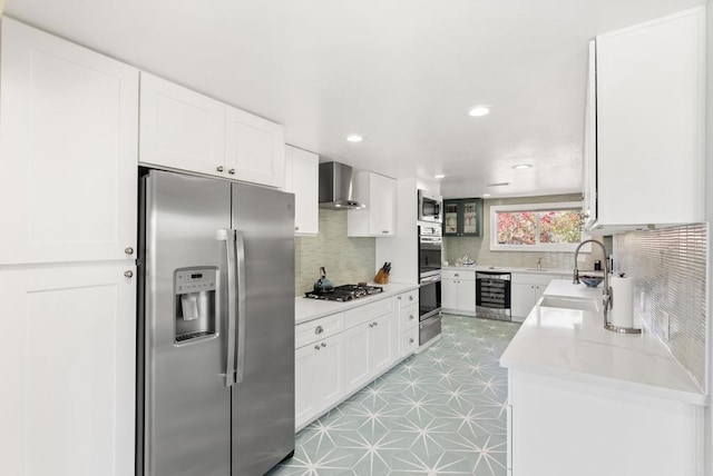 kitchen with appliances with stainless steel finishes, white cabinetry, a sink, and wall chimney exhaust hood