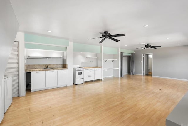 kitchen with white electric stove, light wood-style flooring, a sink, white cabinets, and open floor plan