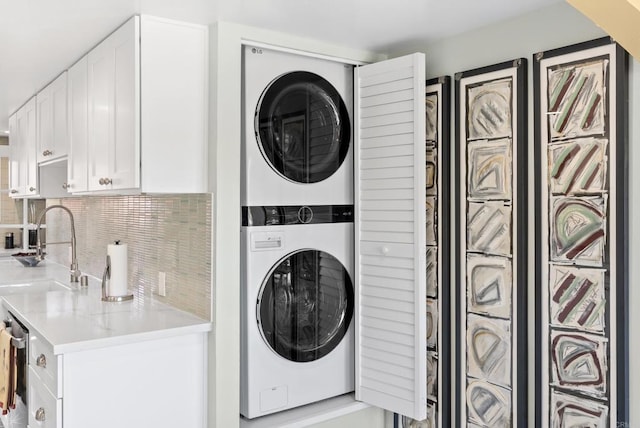 clothes washing area featuring stacked washer and dryer, laundry area, and a sink