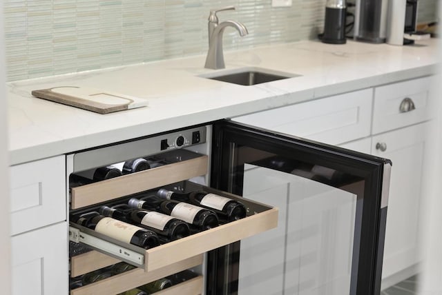 room details with light stone counters, backsplash, white cabinetry, a sink, and beverage cooler