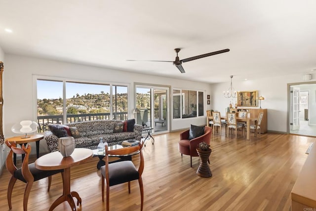 living area featuring ceiling fan with notable chandelier and light wood finished floors