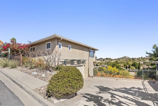 view of side of home with concrete driveway, fence, a garage, and stucco siding