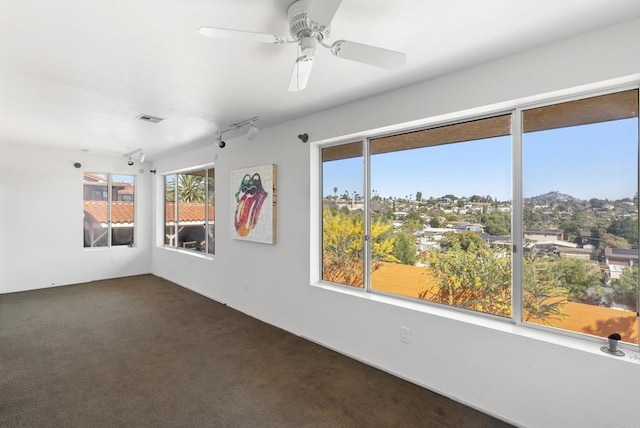 spare room featuring dark carpet, plenty of natural light, visible vents, and a ceiling fan