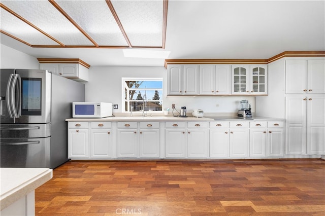 kitchen with stainless steel fridge with ice dispenser, white microwave, glass insert cabinets, light countertops, and white cabinetry