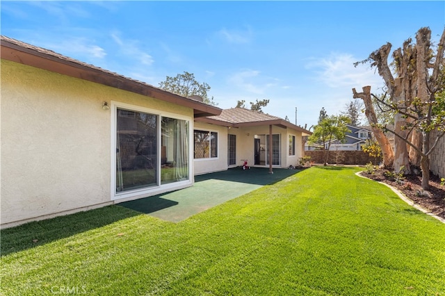 back of house featuring a yard, fence, and stucco siding