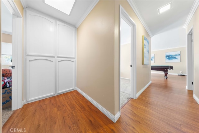 hallway with a skylight, crown molding, light wood-style flooring, and baseboards