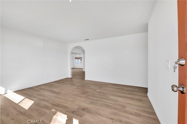 spare room featuring light wood-style floors, arched walkways, visible vents, and baseboards