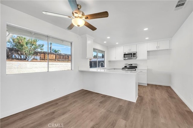 kitchen with baseboards, wood finished floors, stainless steel appliances, light countertops, and white cabinetry