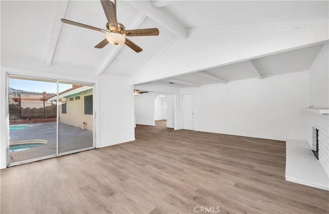 unfurnished living room featuring arched walkways, vaulted ceiling with beams, a fireplace, ceiling fan, and wood finished floors