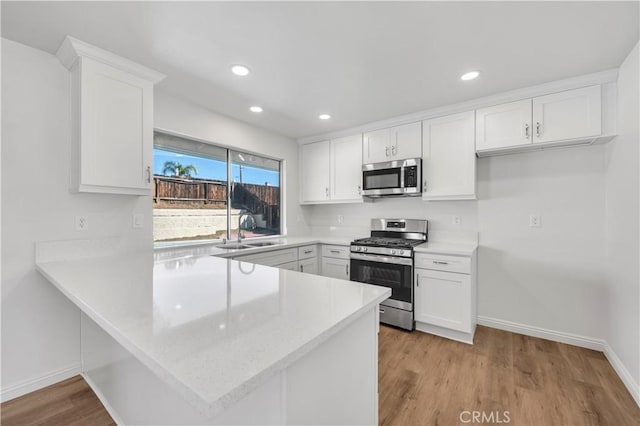 kitchen featuring light countertops, appliances with stainless steel finishes, white cabinetry, a sink, and a peninsula